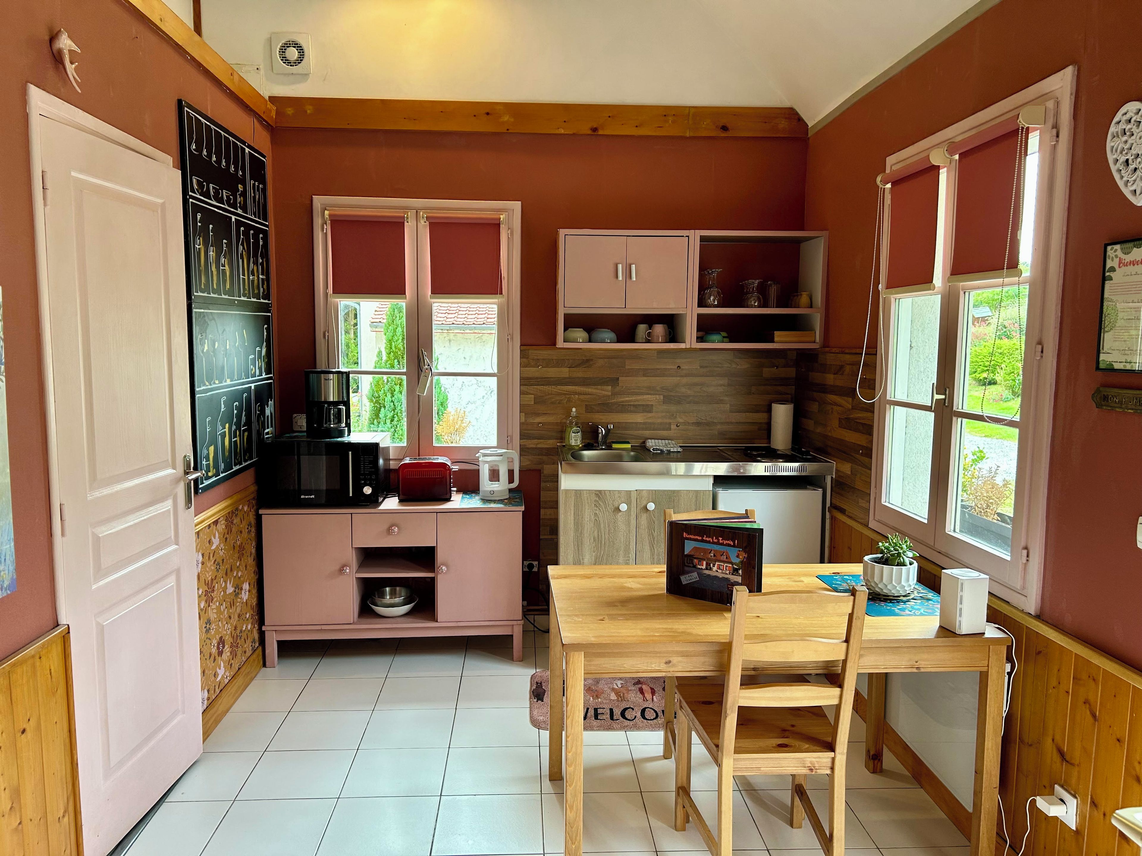 A compact kitchen with a dining area, wooden cabinets, a microwave, a toaster, and a window with a view of greenery.