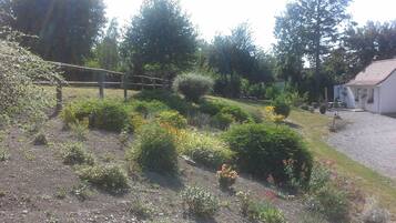 A garden with various plants and flowers, a wooden fence, and a building with a red roof.