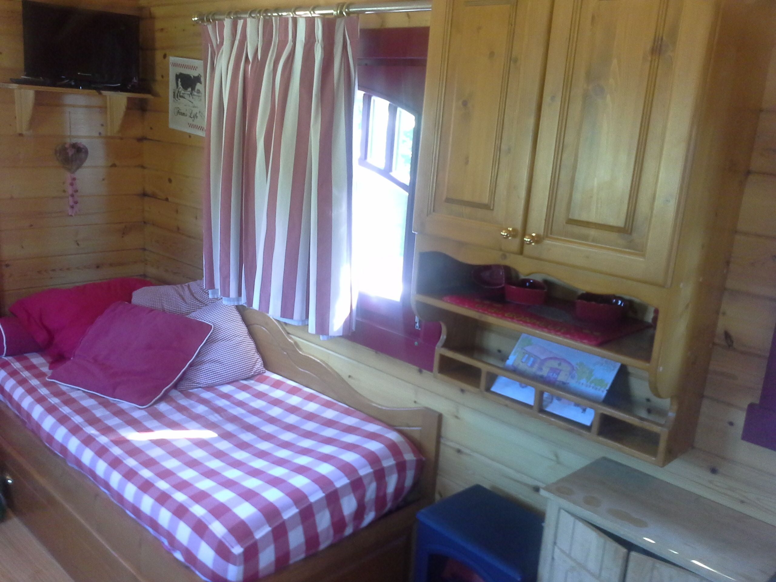 Une pièce de cabane en bois avec un lit à carreaux, une petite table et un placard.