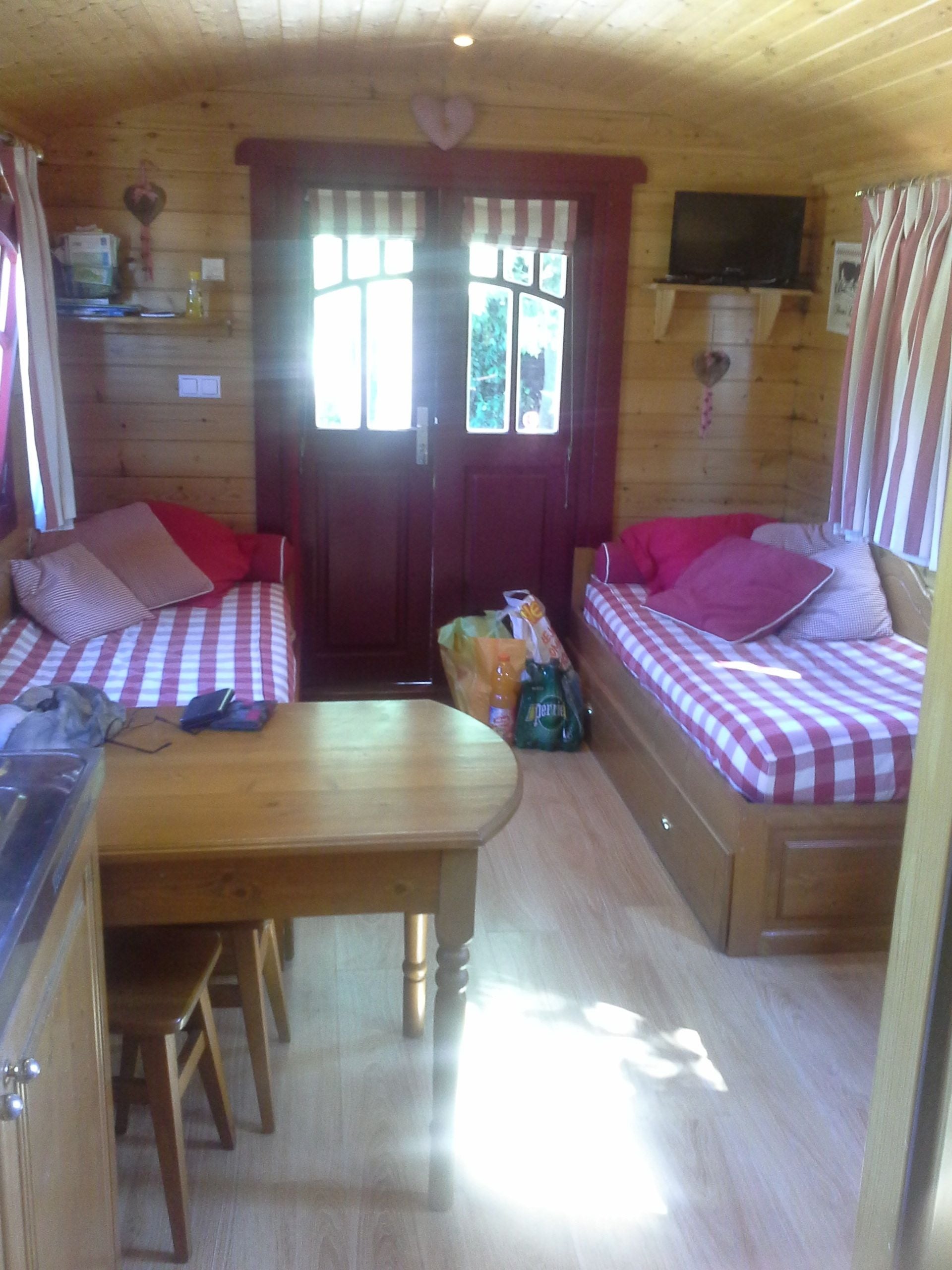 A cozy cabin interior with two wooden beds with checkered bedding, a wooden dining table, and a television mounted on the wall.