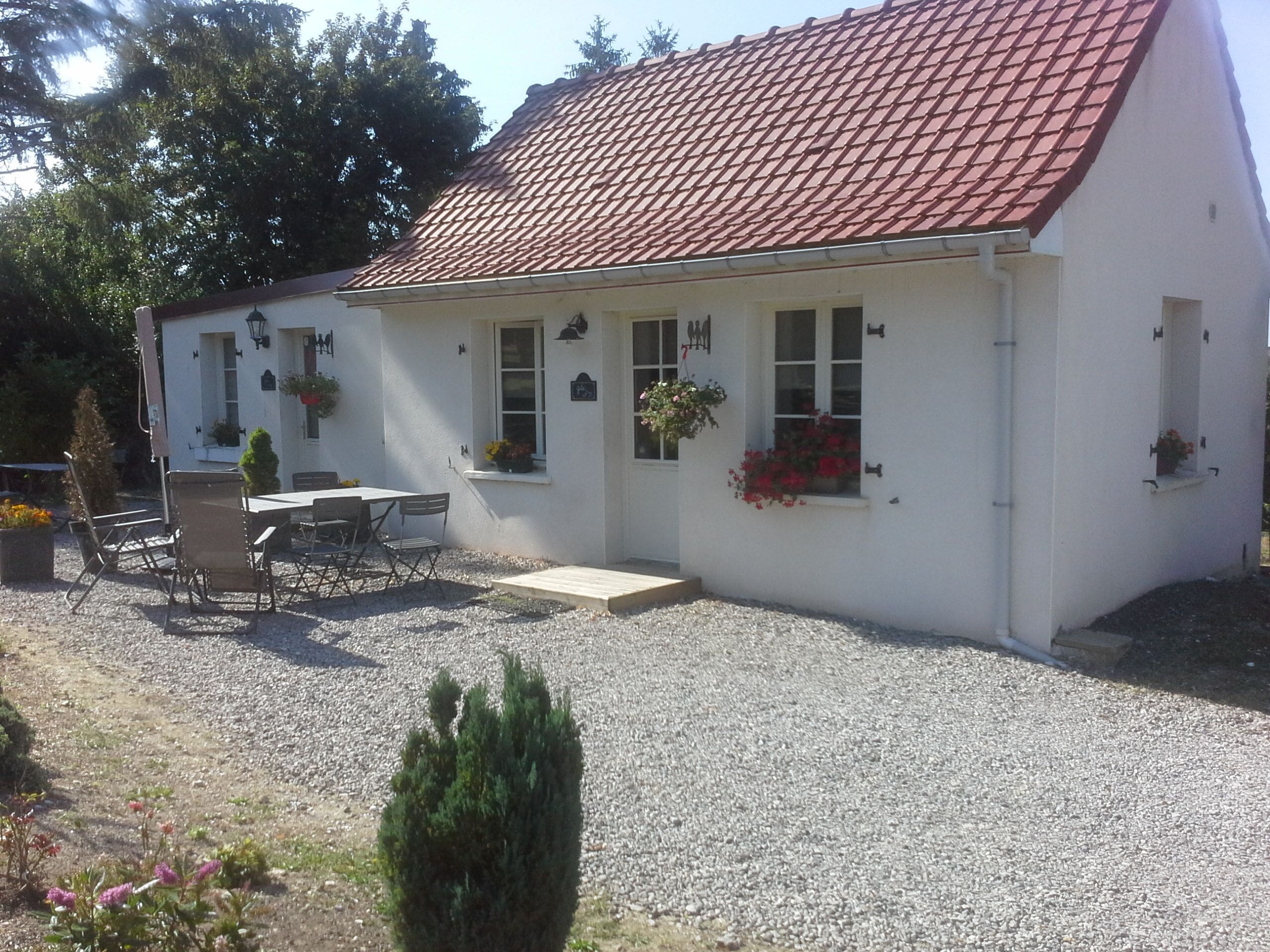 Ein weißes Gebäude mit rotem Ziegeldach, einem Kiesweg und einer kleinen Terrasse mit Tisch und Stühlen.