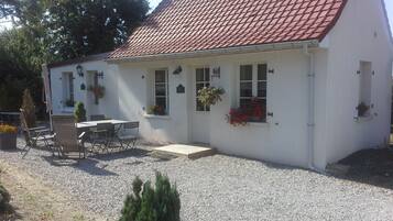 Ein weißes Gebäude mit rotem Ziegeldach, einem Kiesweg und einer kleinen Terrasse mit Tisch und Stühlen.