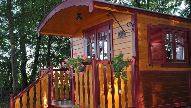 Une maison en bois avec un porche, des volets rouges et une cloche.