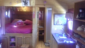 Une chambre confortable, aménagée dans le style d’un chalet, avec un lit, un petit tabouret, une kitchenette et une salle de bain.
