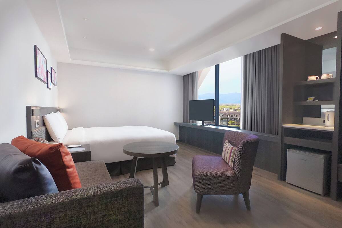 Ett modernt hotellrum med en säng, ett litet runt bord, en stol och en tv.