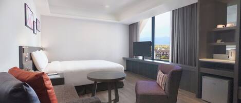 A modern hotel room with a bed, a small round table, a chair, and a TV.