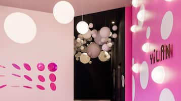 A modern interior with a pink wall and ceiling with hanging spherical lights, and a dark wall with a cluster of lights.