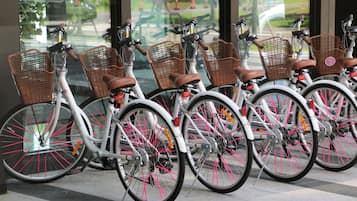 A row of white bicycles with pink spokes and brown baskets, parked in front of a building with large windows.