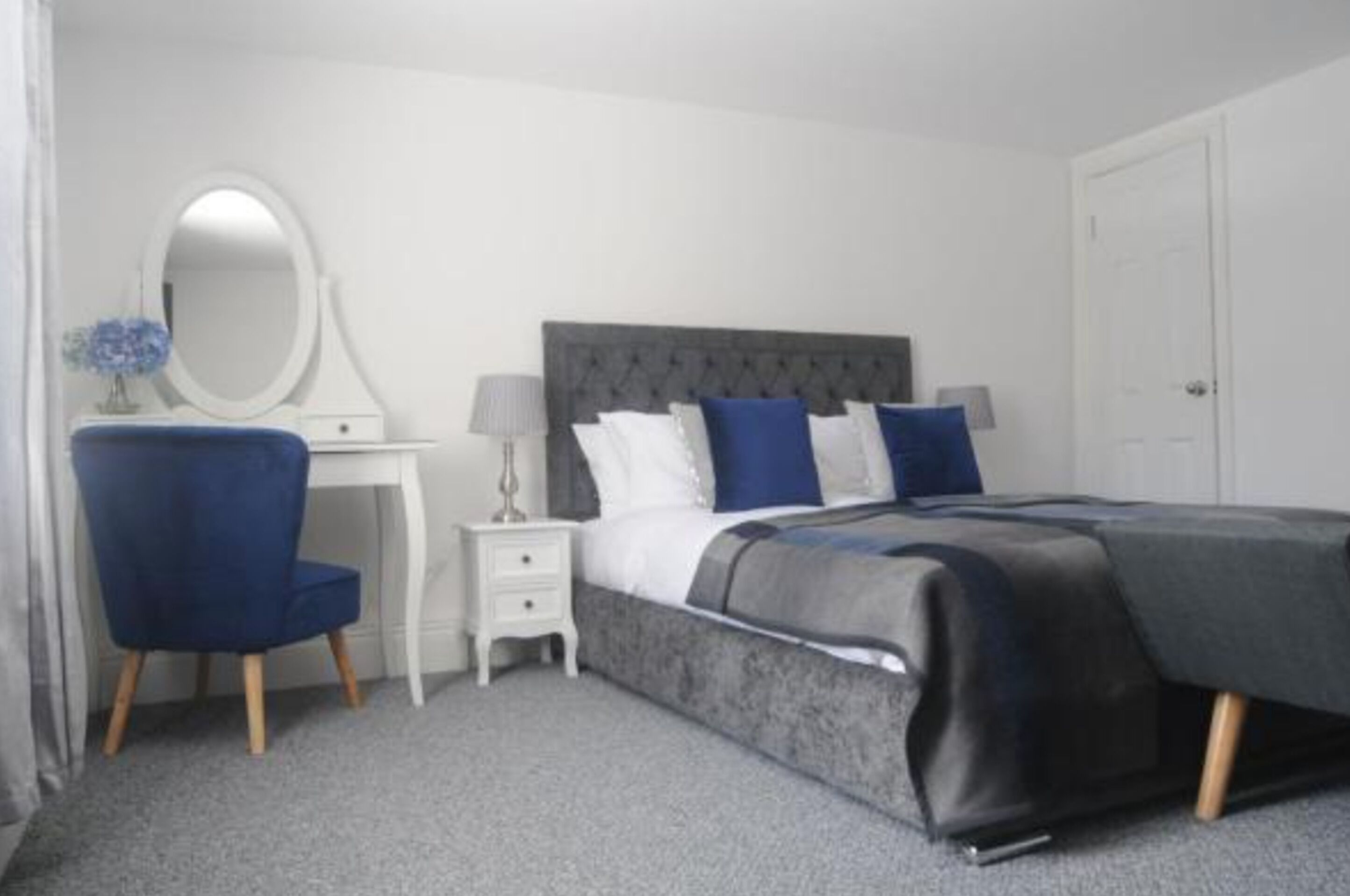 A bedroom with a bed, a dresser, a chair, a mirror, and a nightstand.