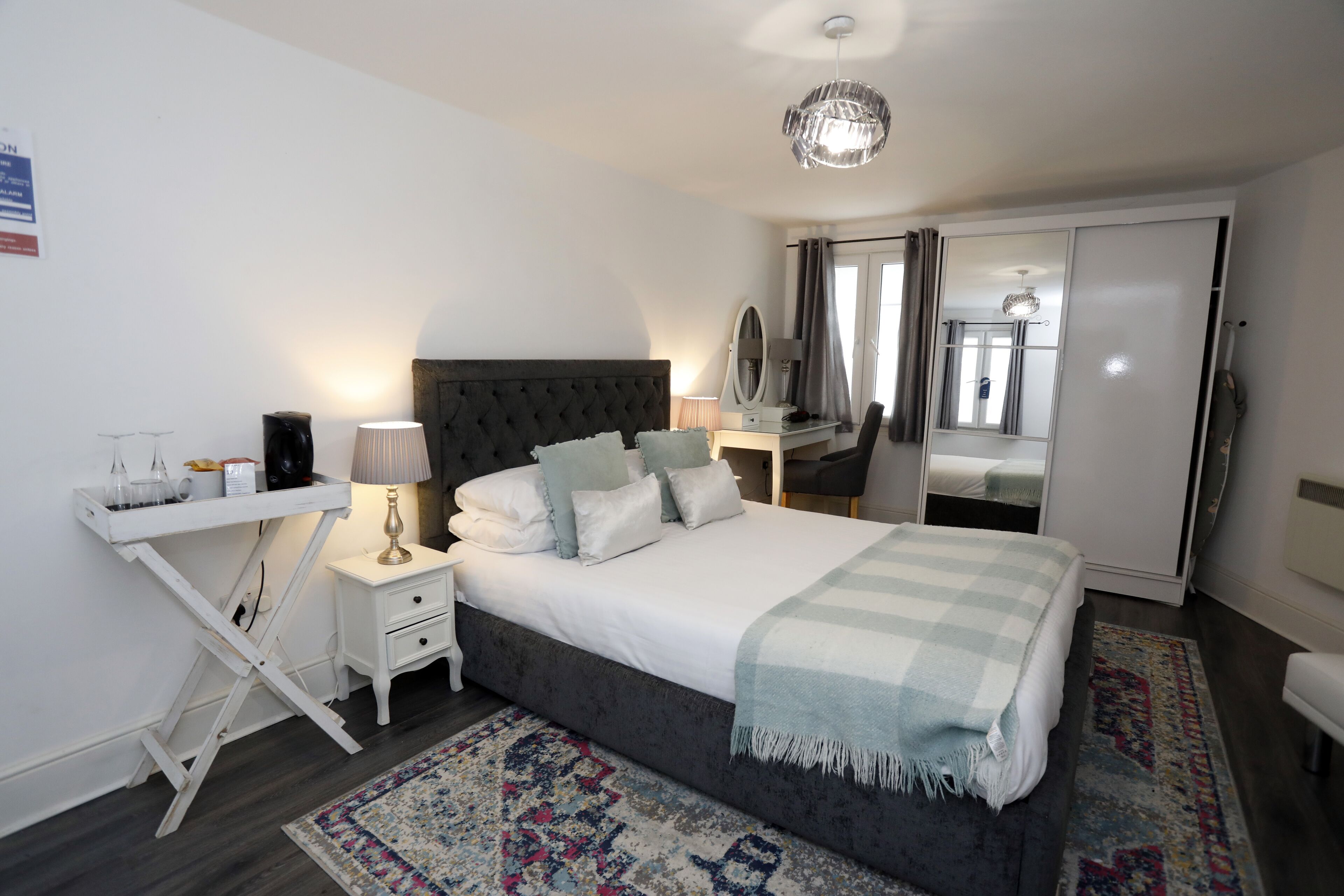 Ein Schlafzimmer mit Bett, Nachttisch, Lampe, Spiegel und Schreibtisch mit Stuhl.