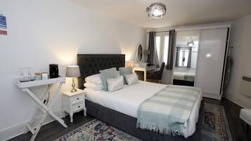 A bedroom with a bed, bedside table, lamp, mirror, and a desk with a chair.