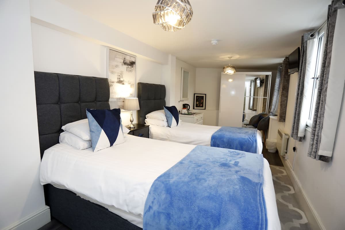 A hotel room with two beds, a large mirror, a chandelier, and a view of the hallway.