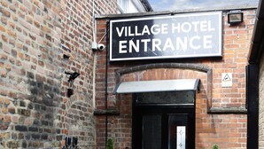 A brick building with a sign reading "Village Hotel Entrance." - Bexley Village Hotel (Bexley)