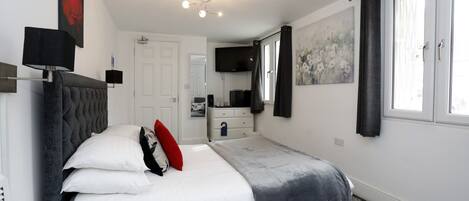 A bedroom with a bed, bedside tables, a TV, a painting, and a window with curtains.