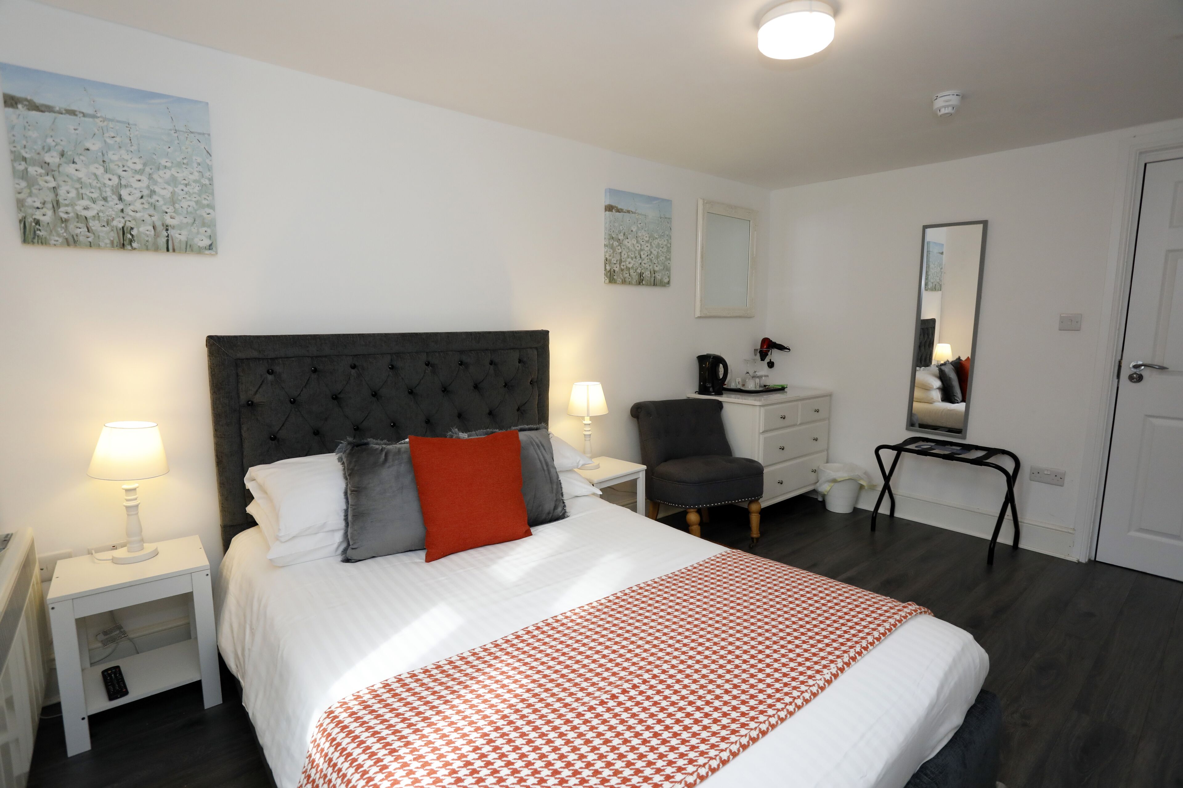 Een slaapkamer met een groot bed, een nachtkastje met een lamp, een stoel, een dressoir en een spiegel.