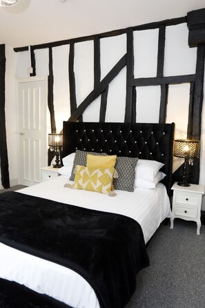 A bedroom with a black and white Tudor-style headboard, a white bed with multiple pillows, two bedside tables with lamps, and a white door. - Bexley Village Hotel (Bexley)