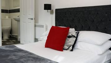 Un dormitorio con cama, almohada roja, almohada blanco y negro, luz empotrada en la pared y un cuadro con una flor roja.