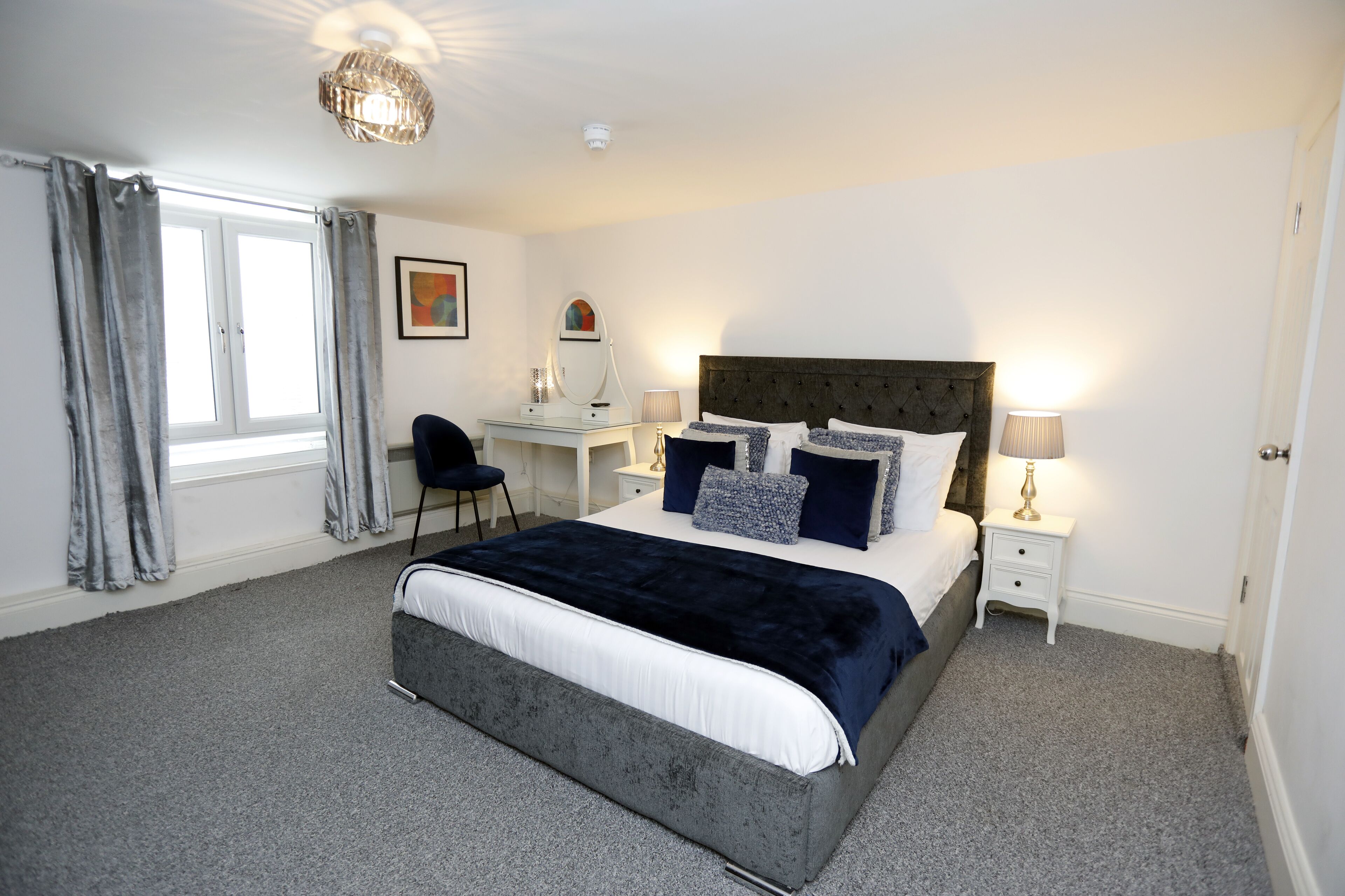 A bedroom with a large bed, a desk, a chair, and a window with curtains.