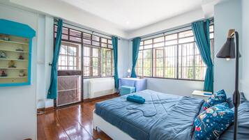 Une chambre avec un grand lit, une petite table, une étagère ornée d’objets décoratifs et une vue par la fenêtre.
