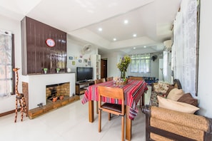 Uma sala de estar ampla com lareira, uma mesa de jantar com toalha vermelha e uma área de estar aconchegante com almofadas.
