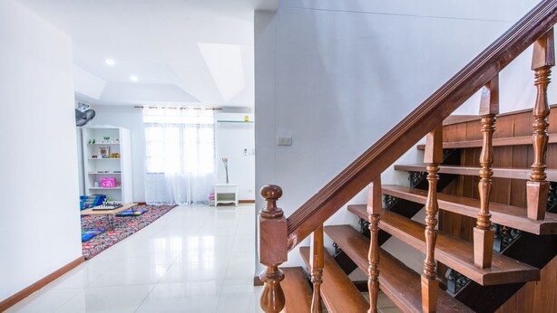 A spacious living area with a wooden staircase, a white wall, and a large window. - Nimman Elegant Garden Villa (Chiang Mai)