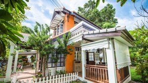 A two-story house with a balcony, a fenced garden, and a small porch with a railing. - Nimman Elegant Garden Villa (Chiang Mai)