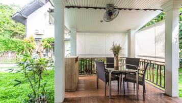 Um alpendre coberto com uma mesa e cadeiras, rodeado por vegetação e vista para um jardim.