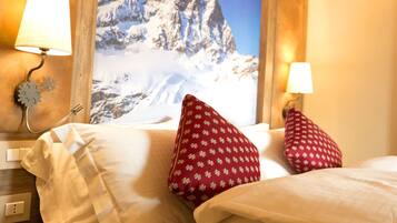 A hotel room with a bed, two red pillows with a snowflake pattern, a wall-mounted lamp, and a mountain view poster.