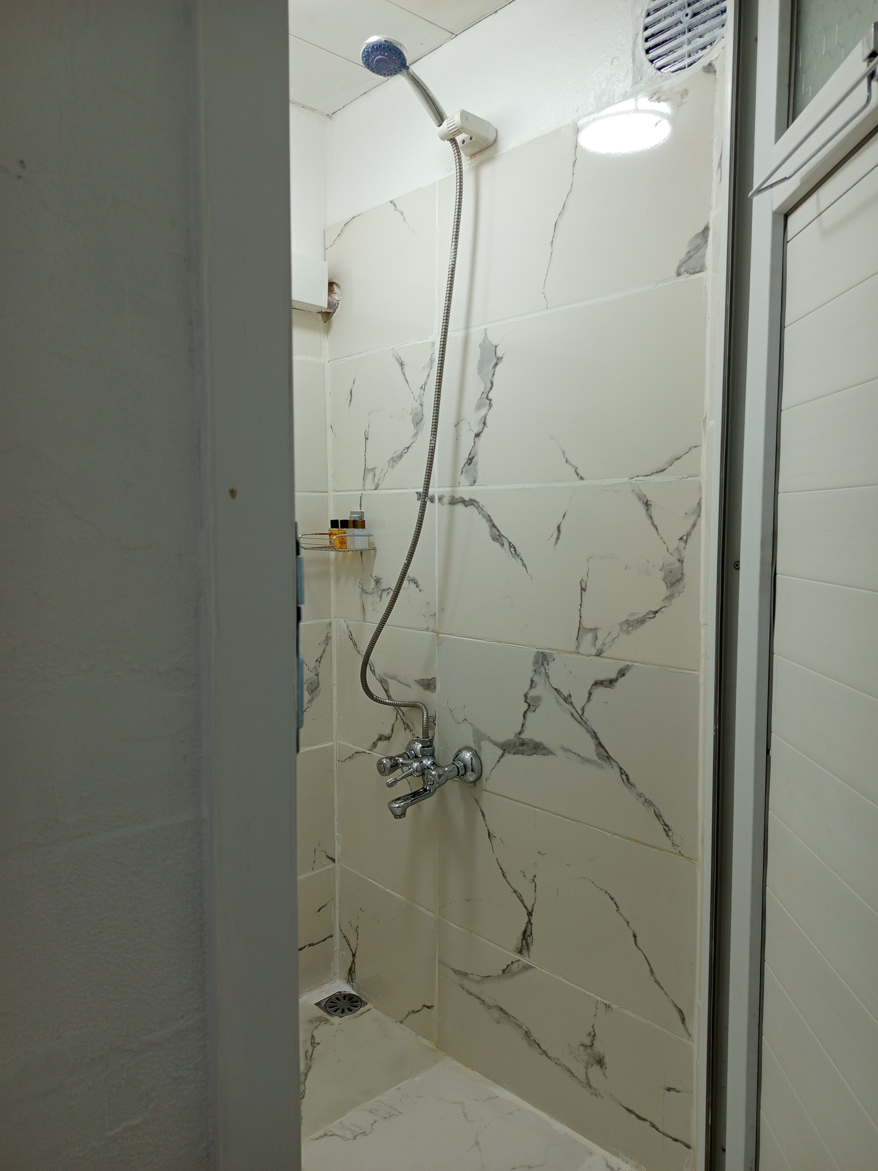 A bathroom with a shower, marble walls, and a glass door.