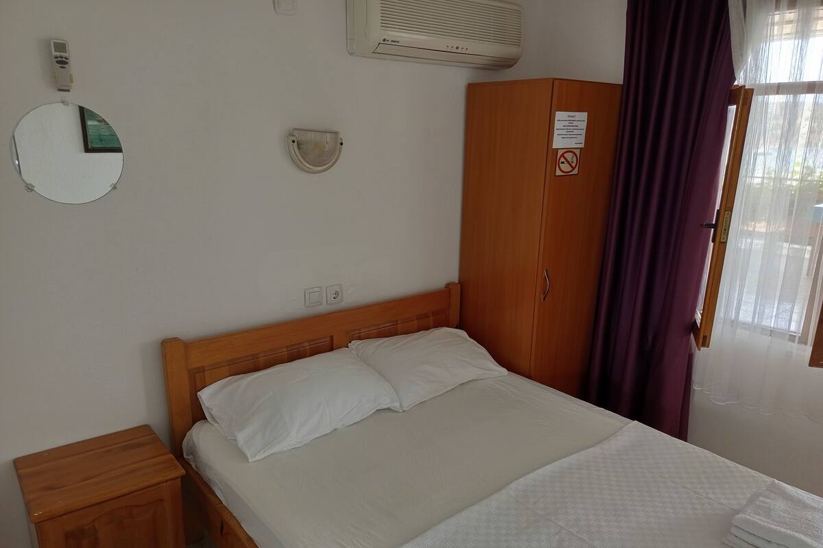A bedroom with a wooden bed, a nightstand, a wardrobe, a mirror, and a window with curtains.