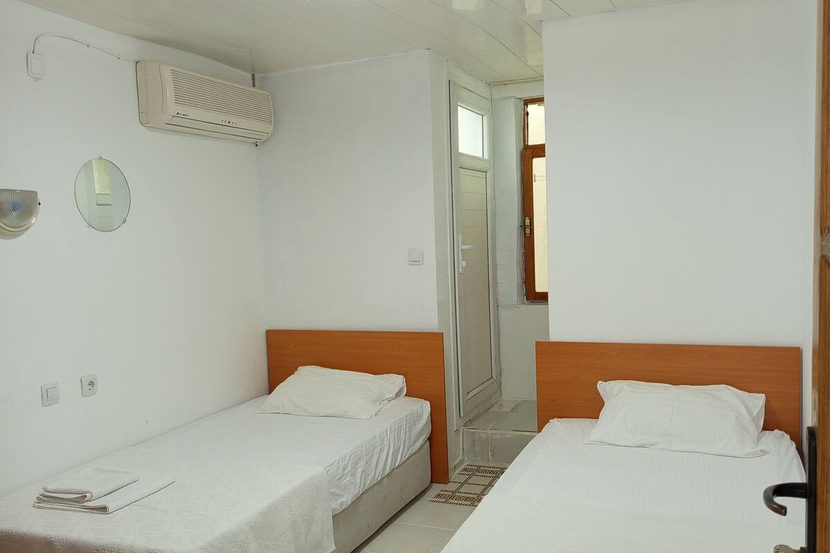 A hotel room with two single beds, a ceiling fan, an air conditioner, and a mirror on the wall.