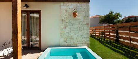A swimming pool with a wooden deck, a stone wall, and a wooden fence in the background.