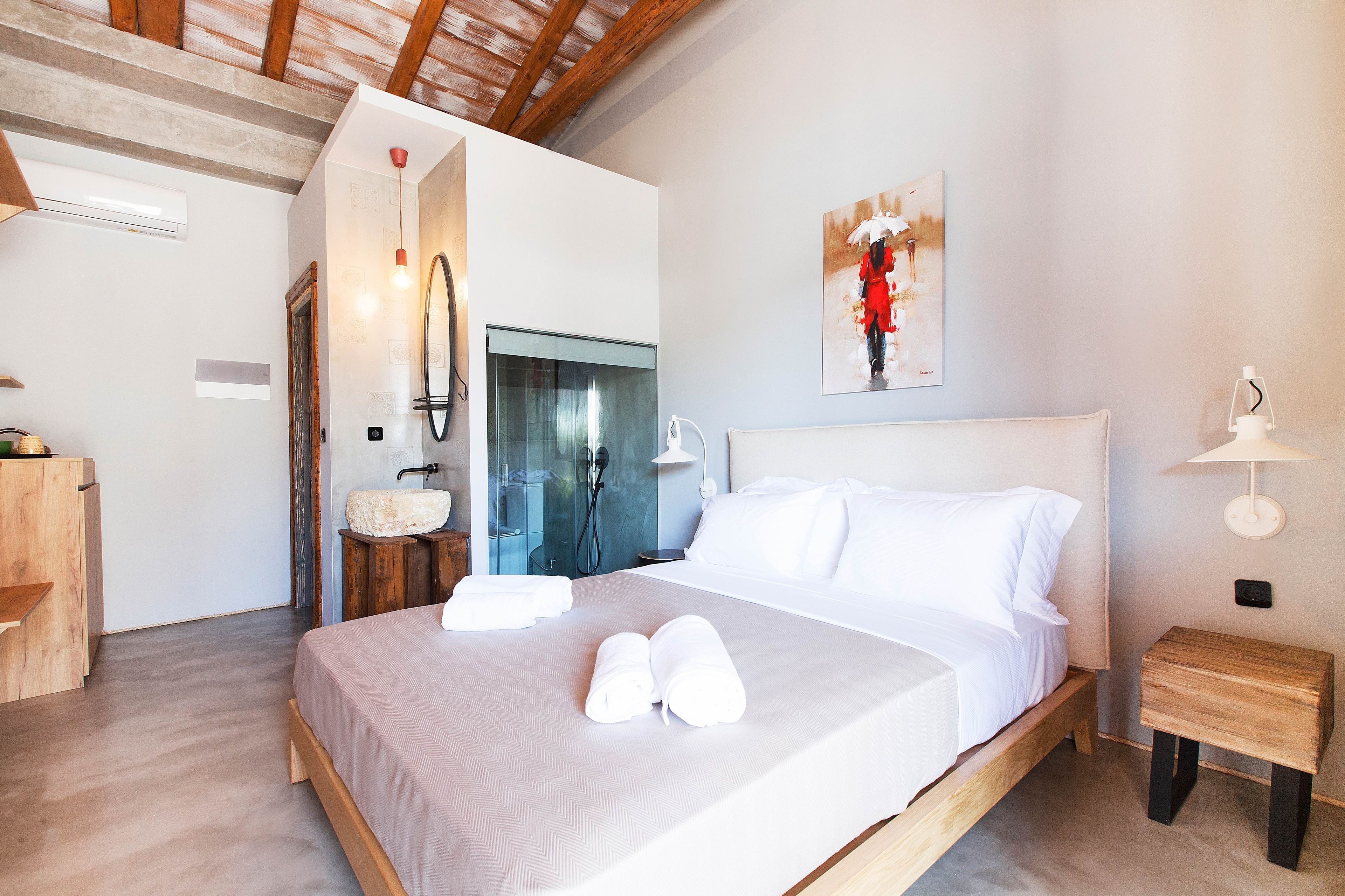 A modern bedroom with a wooden bed, white linens, a wooden nightstand, a mirror, and a painting on the wall.