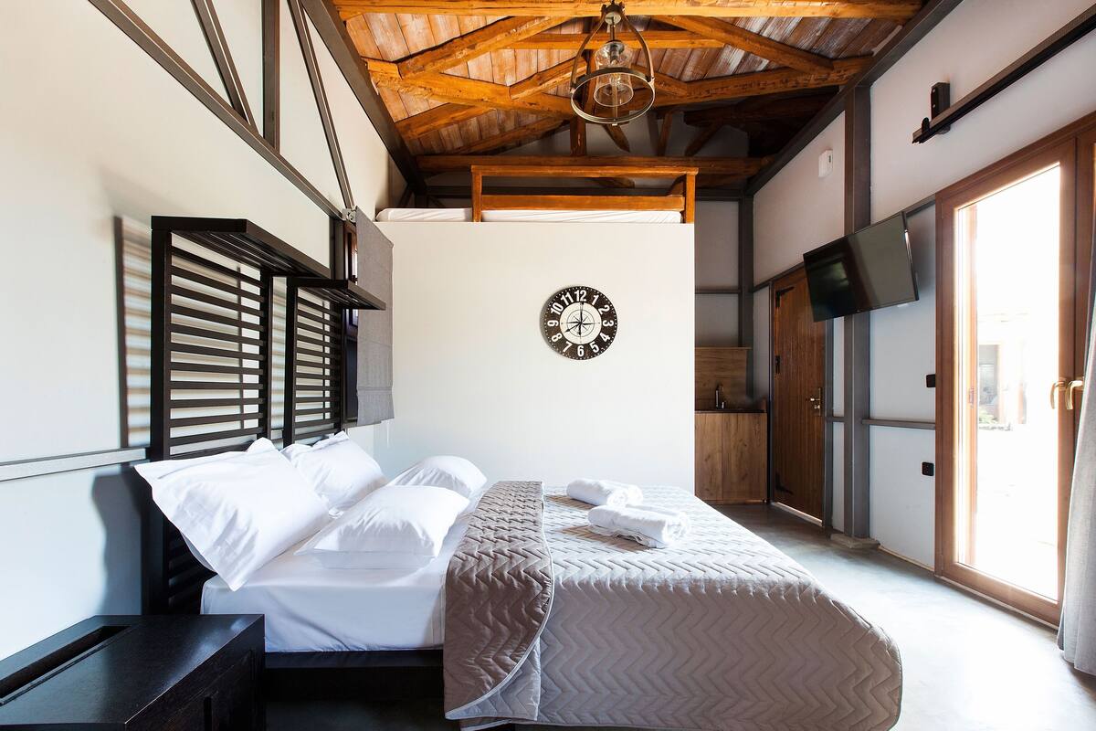 A bedroom with a bed, a clock on the wall, a television, and a sliding door.