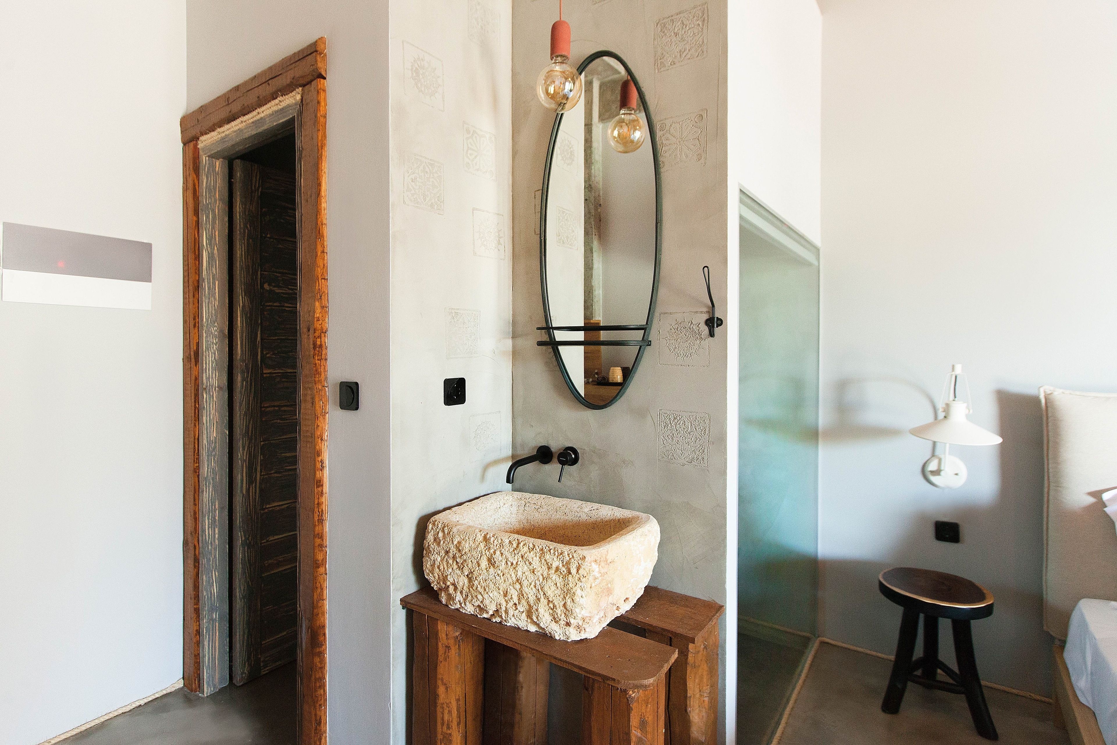 Un baño con lavamanos de piedra, un taburete de madera y un espejo con luces colgantes.