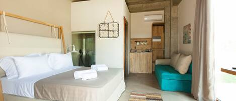 A bedroom with a bed, a wooden headboard, a hanging light fixture, a kitchen area with wooden cabinets, and a teal sofa.