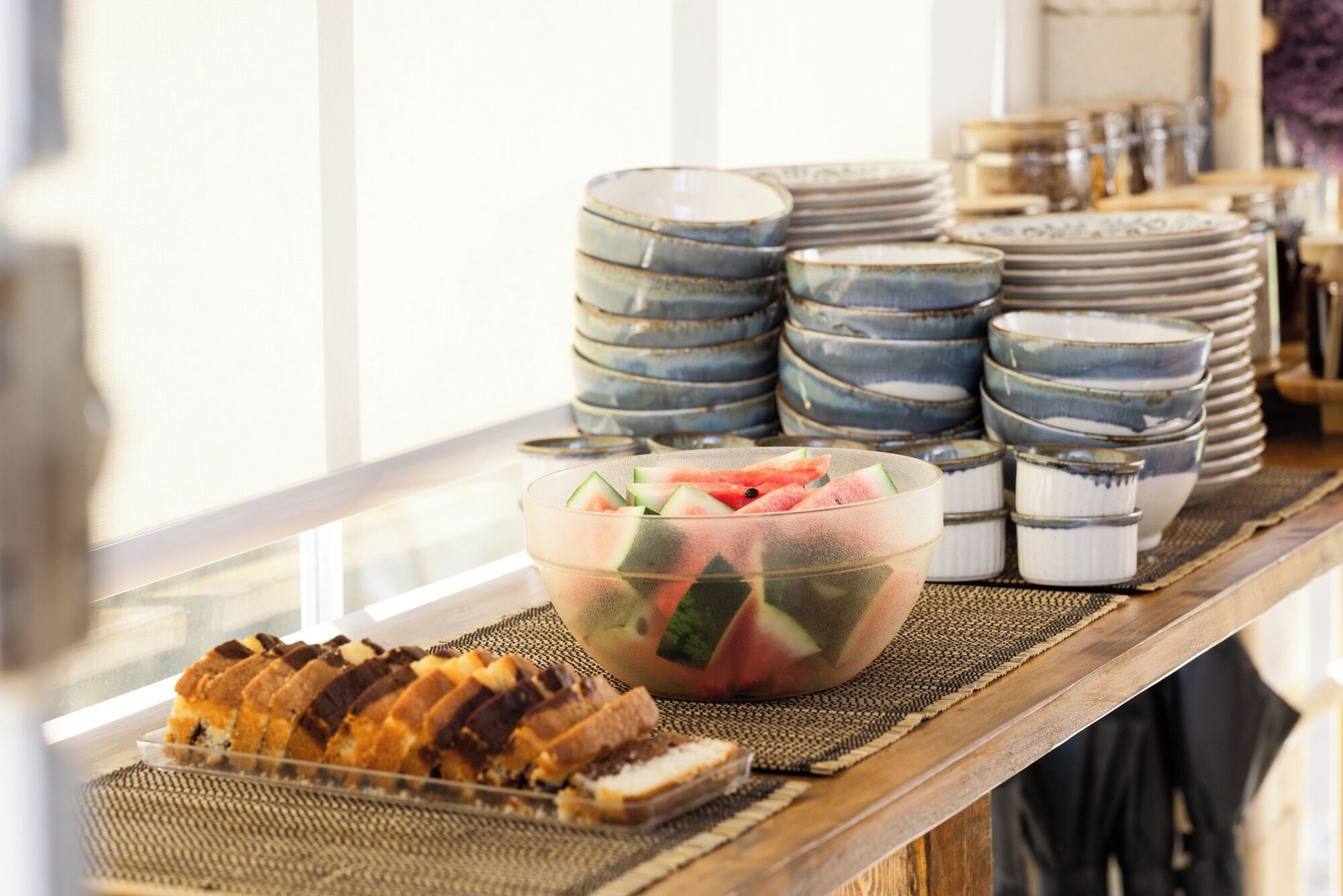 A buffet table with stacked plates and a bowl of fruit salad.