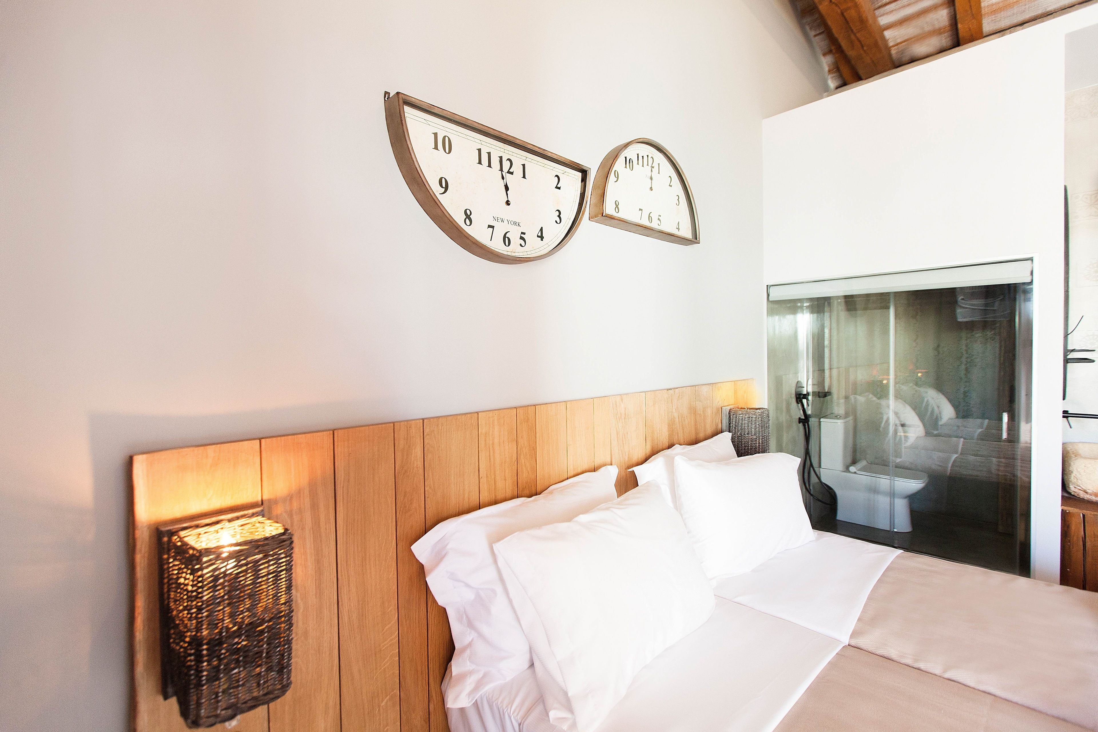 A bedroom with a wooden headboard, a bed with white linens, and two wall clocks.