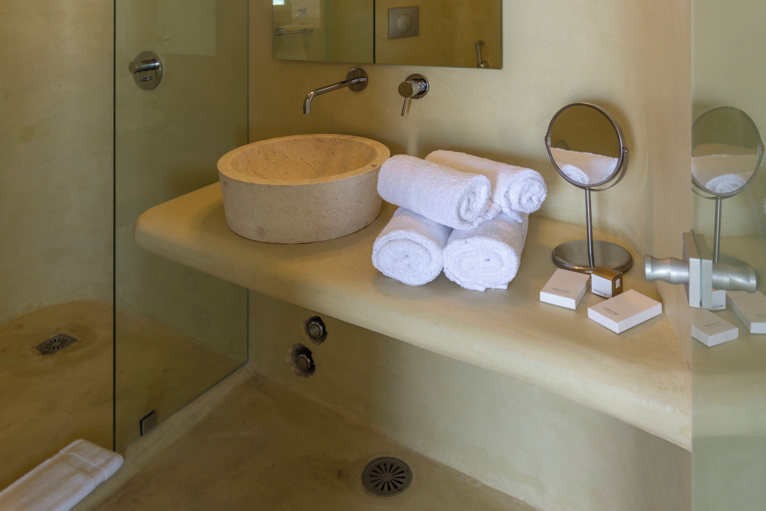 A bathroom with a beige sink, a round mirror, and a glass-enclosed shower.