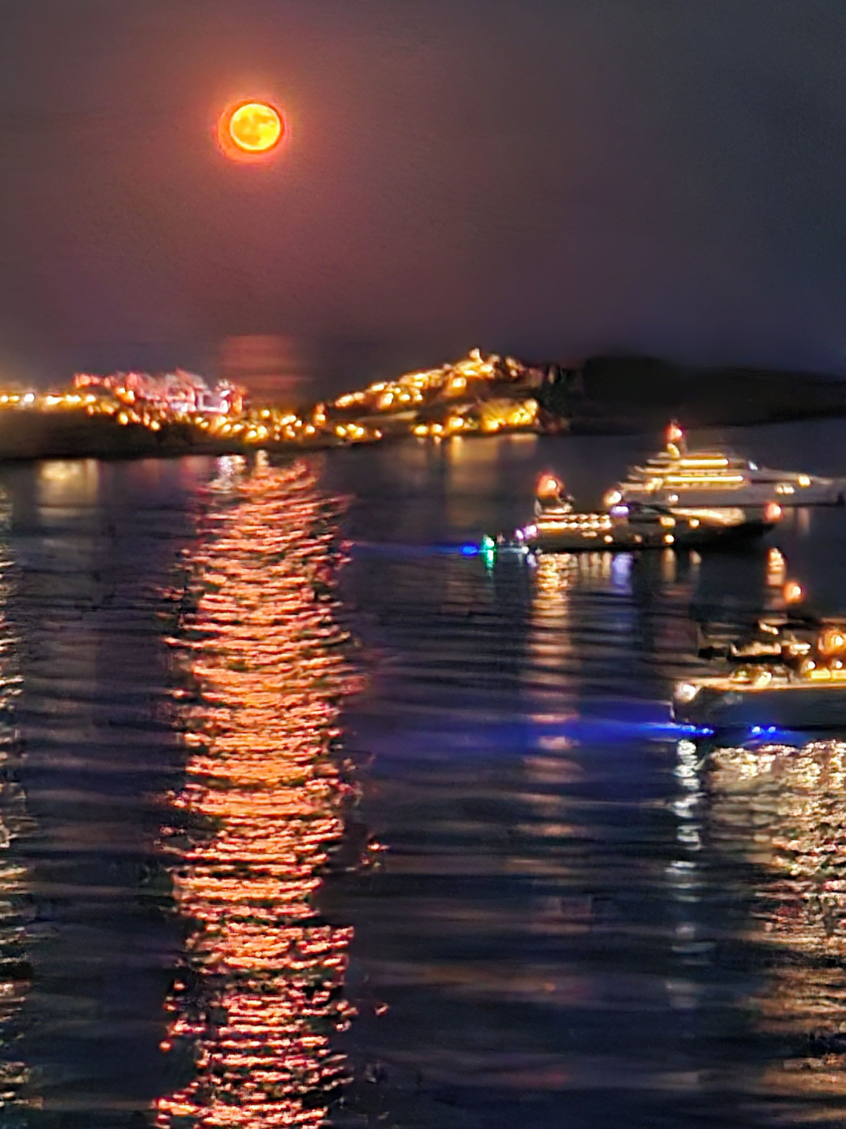 A nighttime harbor scene with boats and city lights reflecting on the water.