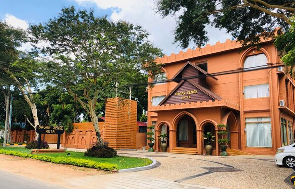 A hotel with a castle-like facade, a signboard, and a well-maintained garden.