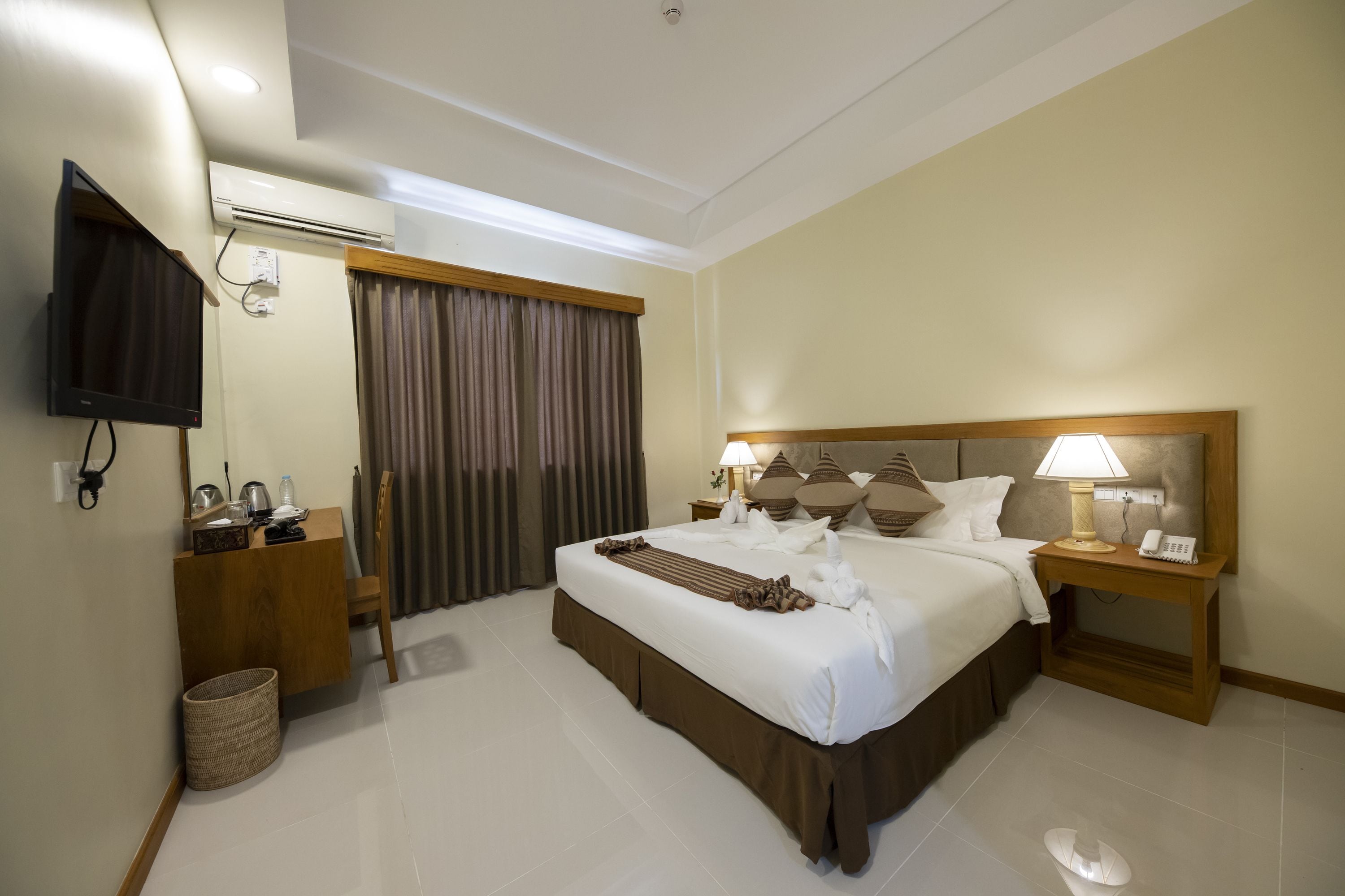 A hotel room with a large bed, a desk, a TV, and a window with curtains.