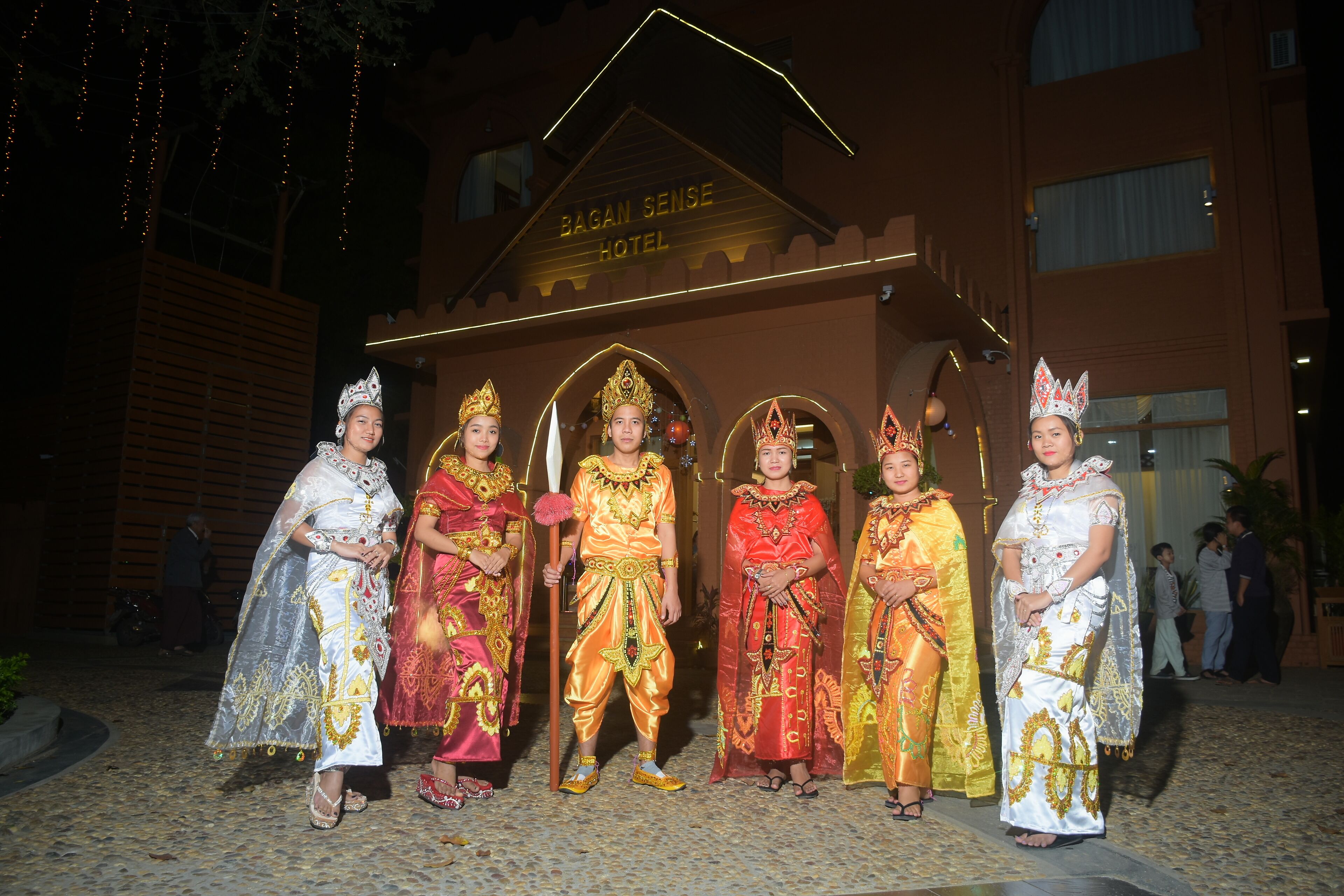 A group of people in traditional attire standing in front of a building with a sign that reads "BAGAN SENSE HOTEL".