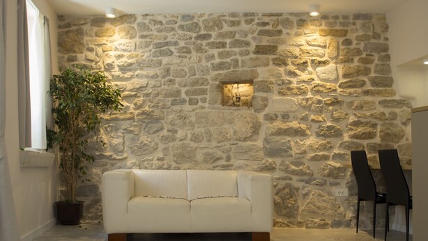 Une pièce avec un mur en pierre, un canapé blanc, deux chaises noires et une plante en pot.