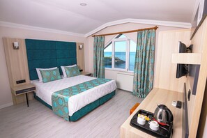 A modern hotel room with a large bed, a small desk with a kettle and cups, and a view of the sea through a window. - Mare Blu Hotel (Akçaabat)