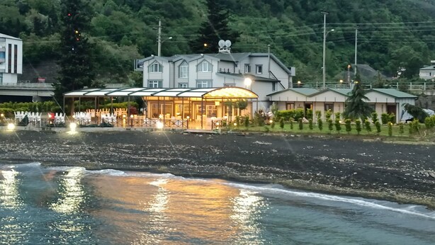A coastal hotel with a beachfront view, a covered outdoor seating area, and a mountainous backdrop. - Mare Blu Hotel (Akçaabat)