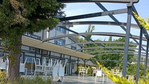 A covered outdoor area with a modern architectural structure, a tiled floor, and white outdoor furniture. - Mare Blu Hotel (Akçaabat)