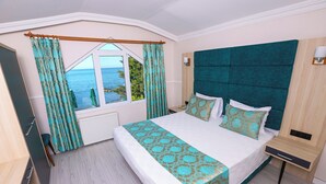 A bedroom with a large bed, a view of the sea through a window, and a wooden nightstand. - Mare Blu Hotel (Akçaabat)