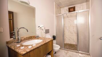 A bathroom with a marble sink, a mirror, a shower with a glass door, and a toilet.