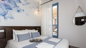 A neatly made bed with a striped bedspread, a tray with breakfast items, and a large mirror on the wall. - Blue Jasmine Suites (Rhodes)